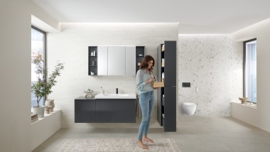 Frau öffnet Hochschrank mit viel Stauraum im Badezimmer mit Badmöbeln der Badserie Geberit Acanto